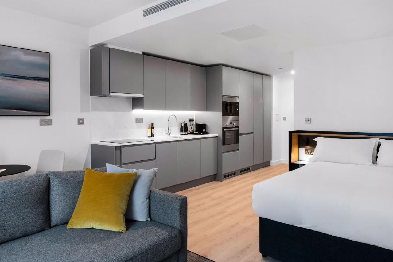 Citysuites 2 Aparthotel Salford  Exterior foto The photo shows a modern studio apartment featuring an open-plan layout. On one side, there is a kitchenette with sleek, gray cabinets and appliances, including a coffee maker and oven. Adjacent to the kitchenette is a small dining area with a table 