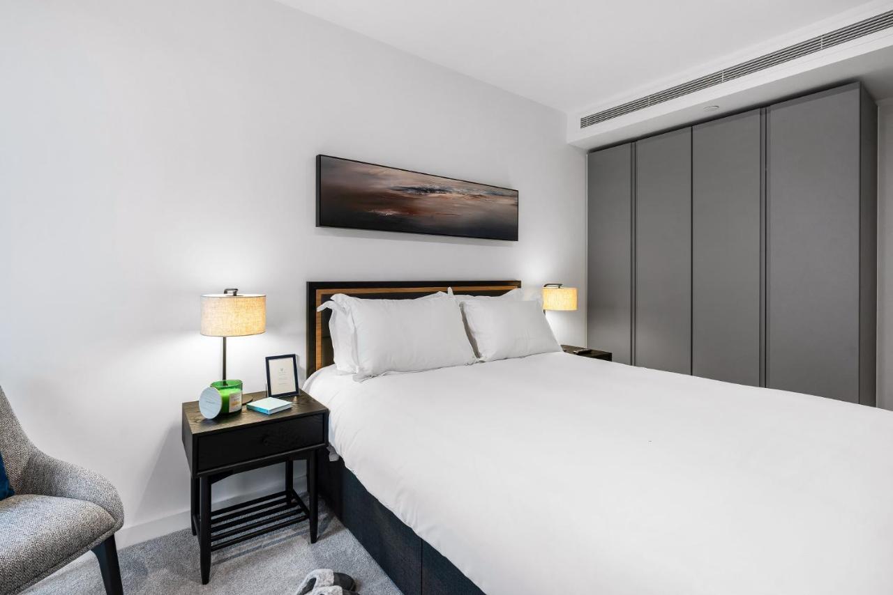 Citysuites 2 Aparthotel Salford  Exterior foto The photo shows a modern bedroom with a neatly made bed featuring white linens and pillows. Flanking the bed are two bedside tables, each with a lamp providing soft lighting. There is a piece of artwork above the bed, which appears to depict a landsc