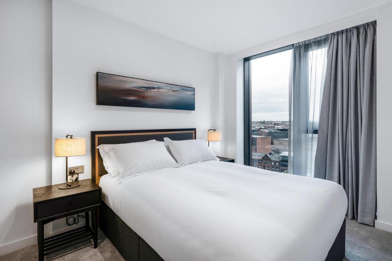 Citysuites 2 Aparthotel Salford  Exterior foto The image shows a modern bedroom featuring a large bed with a white duvet and two pillows. On either side of the bed are small nightstands with lamps. A large window occupies one wall, draped with light gray curtains, allowing natural light to enter 