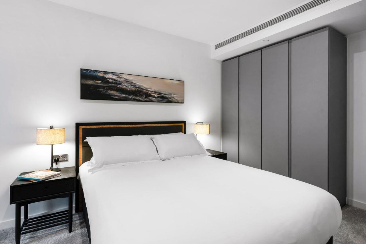 Citysuites 2 Aparthotel Salford  Exterior foto The photo shows a modern bedroom designed with a minimalist aesthetic. The focal point is a large bed with white bedding, positioned against a wall. On either side of the bed, there are black nightstands topped with lamps, providing a warm glow. Abov