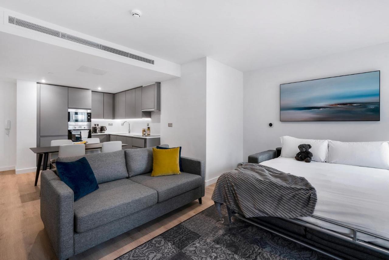 Citysuites 2 Aparthotel Salford  Exterior foto The photo shows a modern, open-concept living space that includes a kitchen and a sleeping area. 

- **Living Area**: On the left, there's a gray sofa with a blue and yellow throw pillow. A blanket is draped over one side, and there's a small dark ru