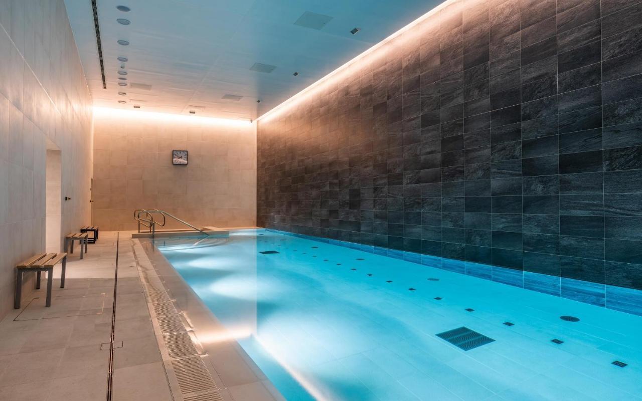 Citysuites 2 Aparthotel Salford  Exterior foto The photo shows an indoor swimming pool area. The pool is illuminated with a soft blue light, creating a calming atmosphere. The walls are designed with dark tiles, and there is a lighter tiled area surrounding the pool. Ambient lighting is installed