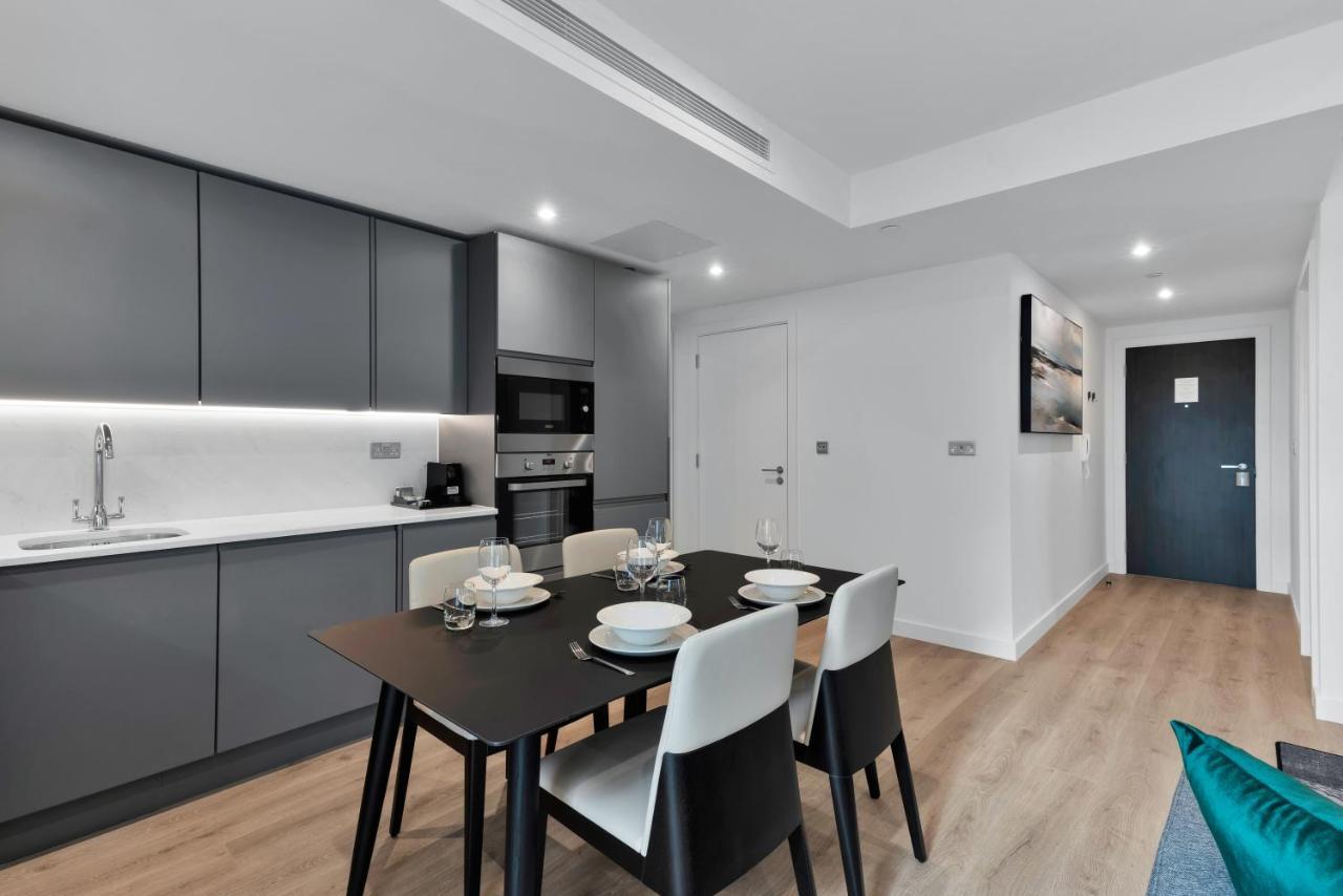 Citysuites 2 Aparthotel Salford  Exterior foto The image shows a modern kitchen and dining area. The kitchen features sleek gray cabinets with a white countertop, and it is equipped with appliances such as a microwave. There’s a dining table set for four, with white plates and glasses ready. The 