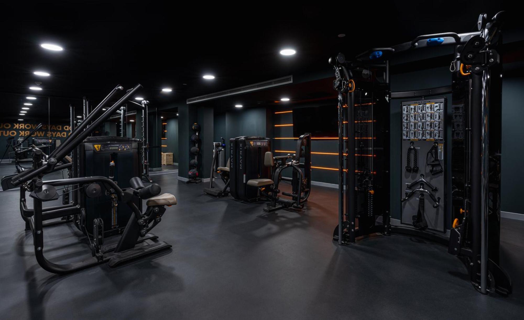 Citysuites 2 Aparthotel Salford  Exterior foto The photo shows a modern gym or fitness area with various workout machines. The space has a dark color scheme, featuring black walls and flooring. There are multiple pieces of exercise equipment, including stations for strength training, possibly tar
