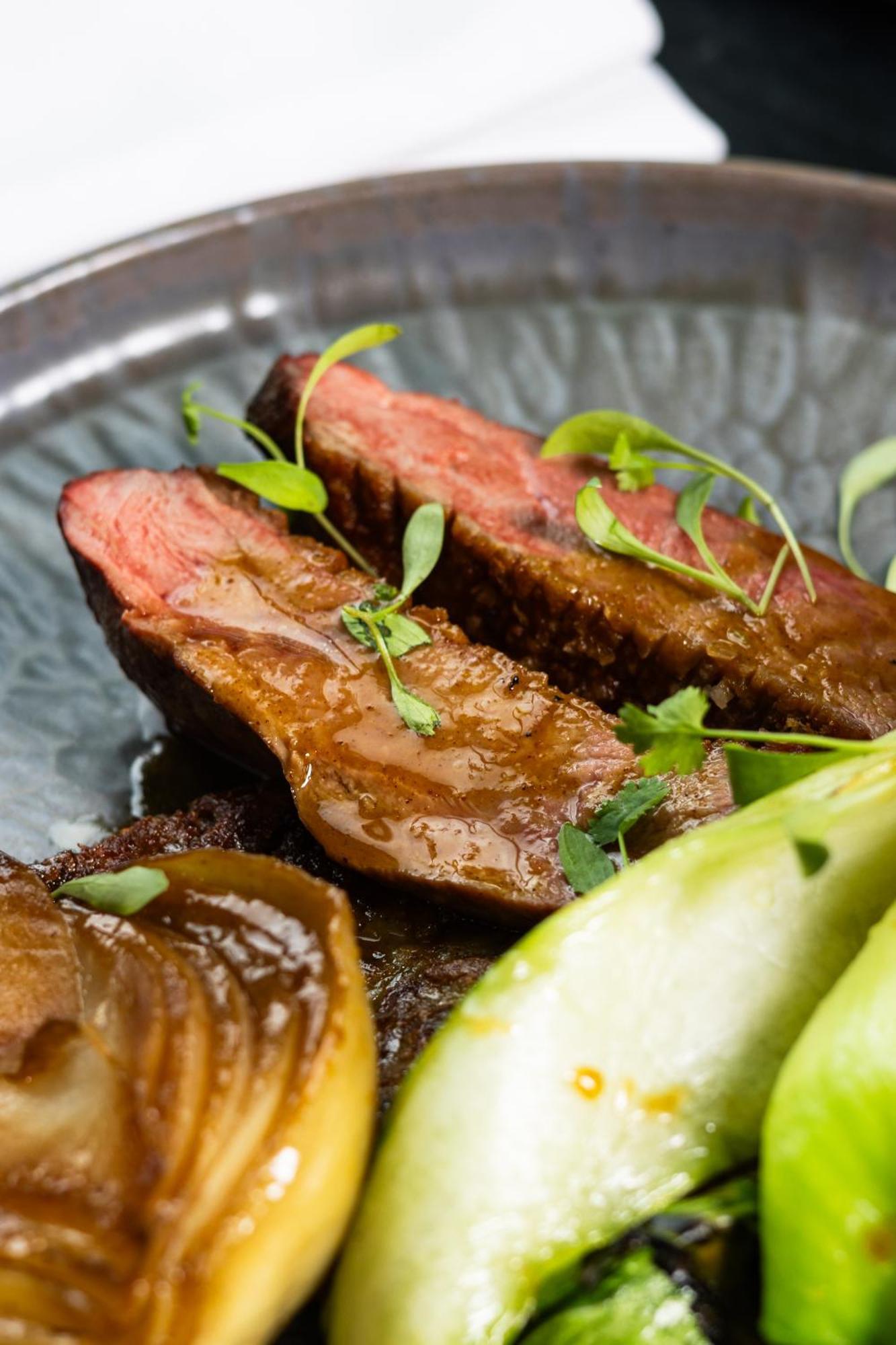 Citysuites 2 Aparthotel Salford  Exterior foto The photo features slices of meat, likely beef, presented on a decorative plate. The meat appears to have a rich brown sauce drizzled over it and is garnished with fresh herbs, adding a pop of green. There are also some slices of a light-colored vege