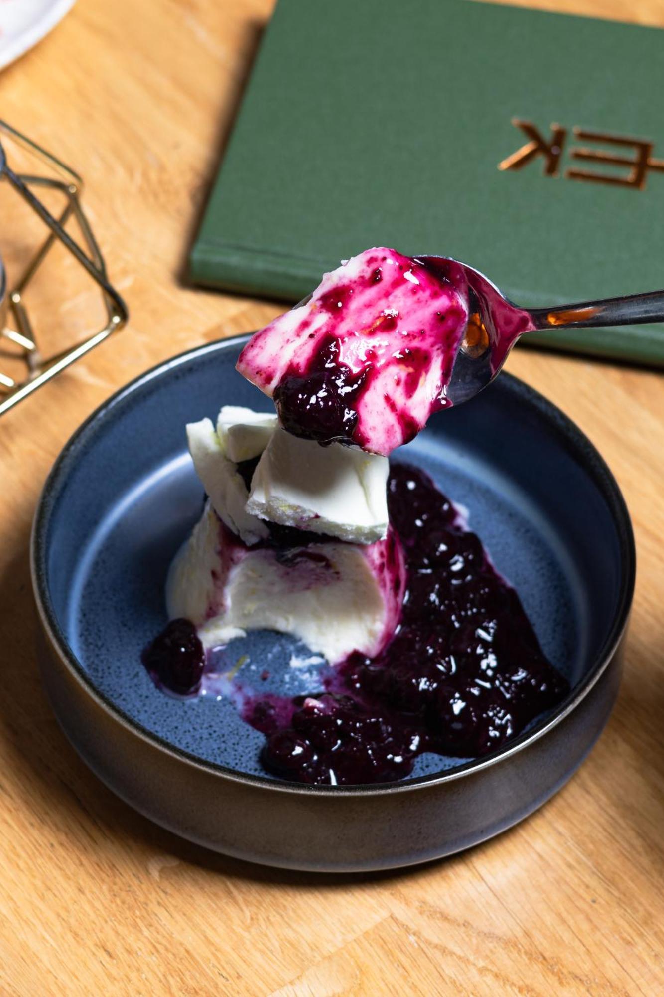 Citysuites 2 Aparthotel Salford  Exterior foto The photo shows a serving of dessert, likely a type of panna cotta or a creamy custard, partially dished out and accompanied by a rich berry sauce, possibly made from blueberries or blackberries. A spoon with some of the dessert and sauce is hovering