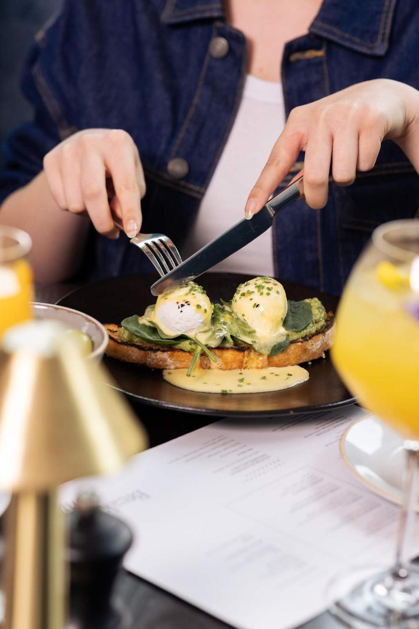 Citysuites 2 Aparthotel Salford  Exterior foto The photo shows a person preparing to eat a dish of eggs Benedict. They are holding a knife and fork, ready to cut into the meal, which features poached eggs on top of a slice of toast, accompanied by spinach and a creamy hollandaise sauce drizzled o