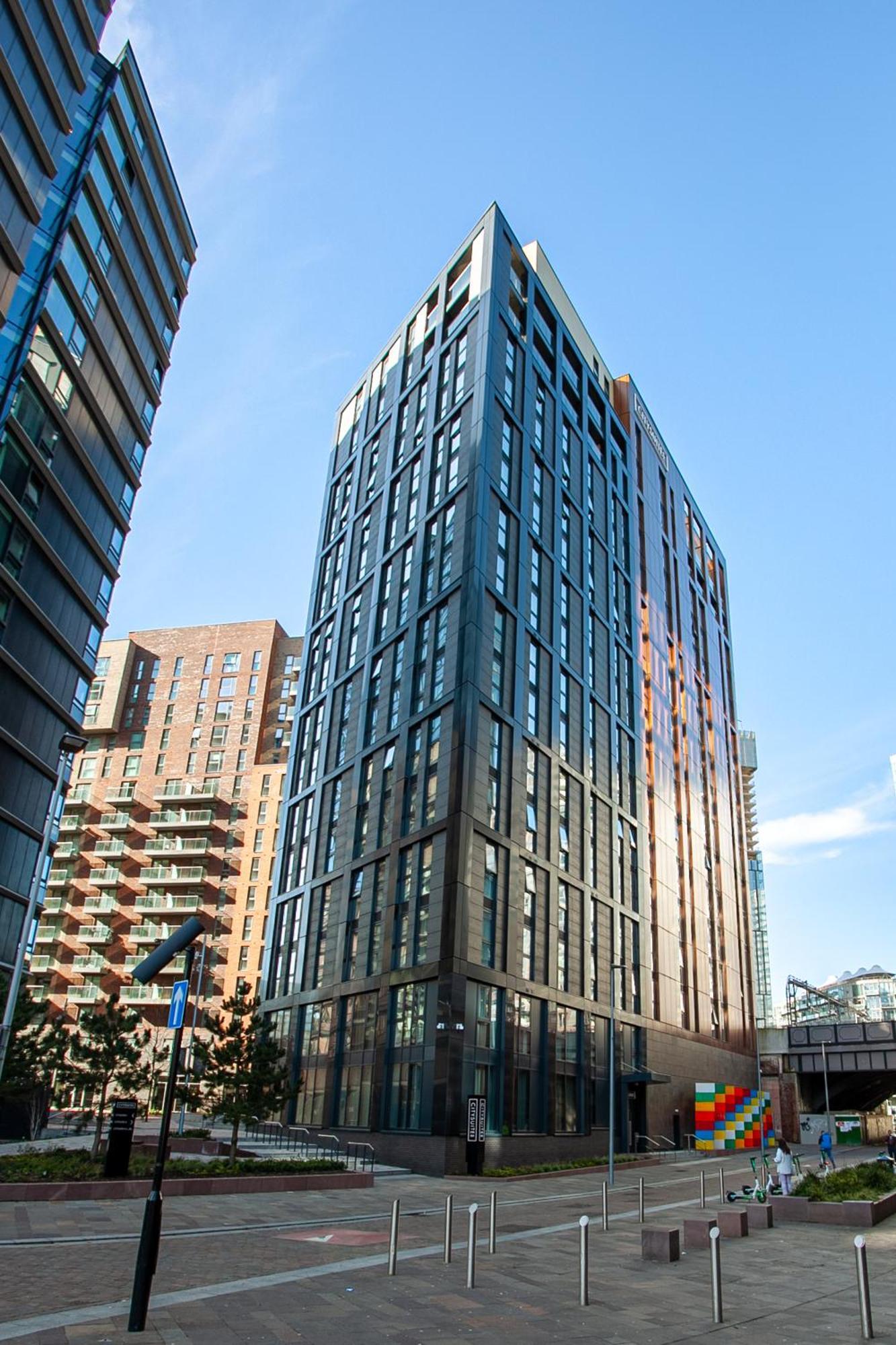 Citysuites 2 Aparthotel Salford  Exterior foto The photo shows a modern high-rise building with a sleek, glass façade. It is set against a blue sky, indicating a clear day. The building appears to have multiple floors with large windows that reflect light. Nearby, there are additional buildings, 